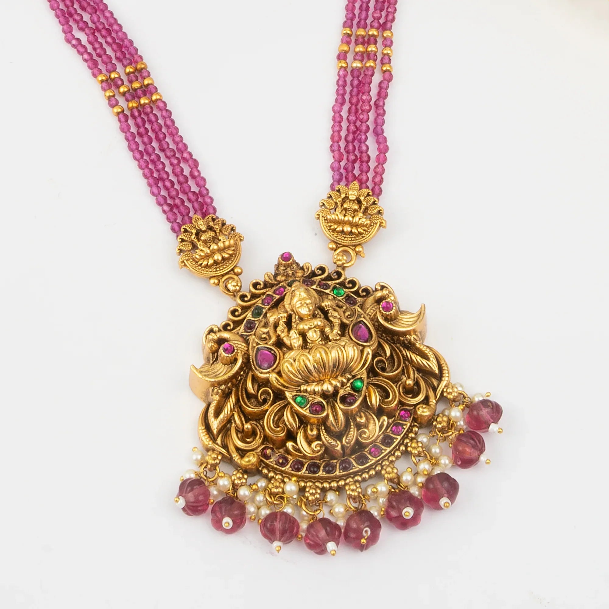 Gold necklace with pink beads and intricate pendant on a white background