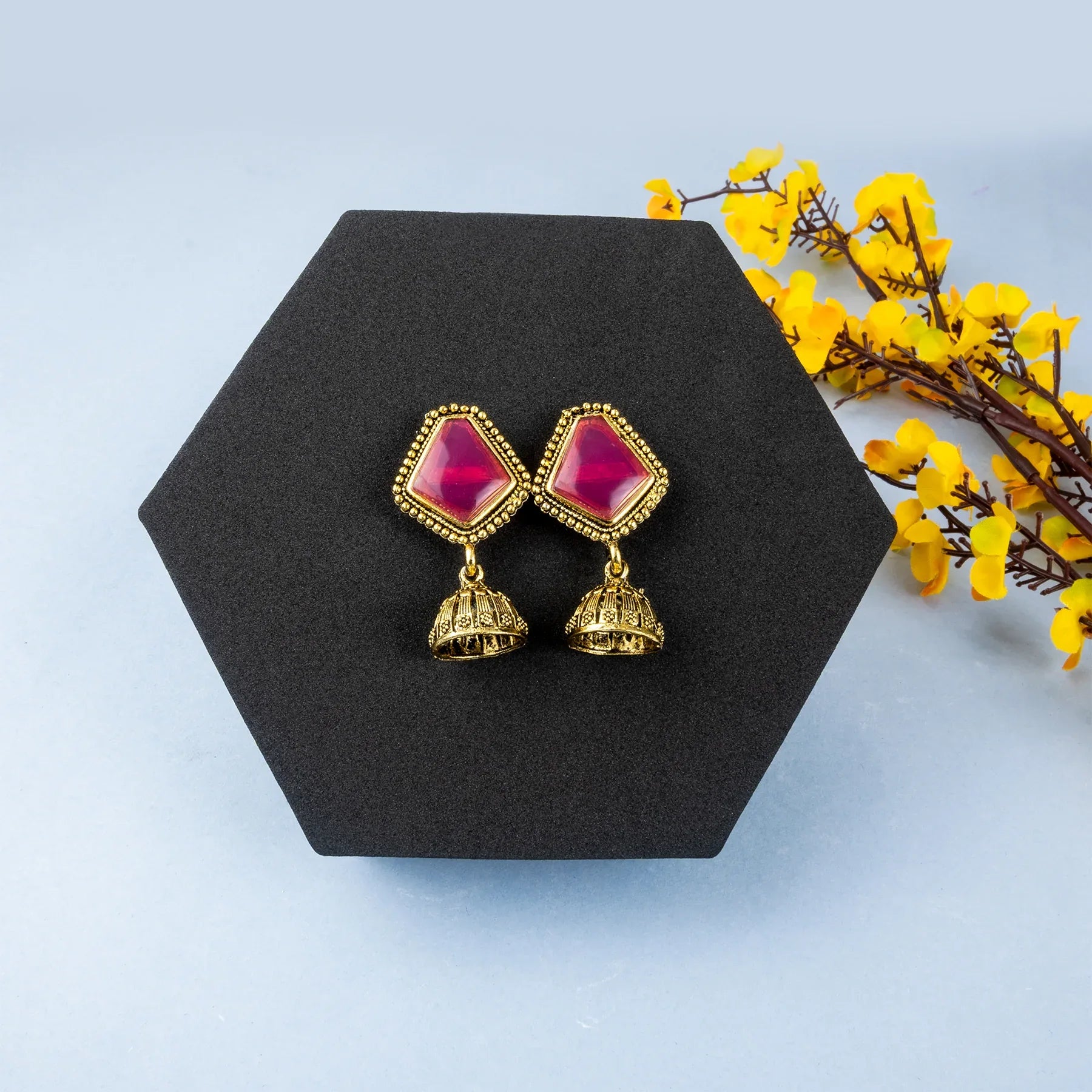 Gold earrings with pink gemstones on a black stand with yellow flowers on a light blue background
