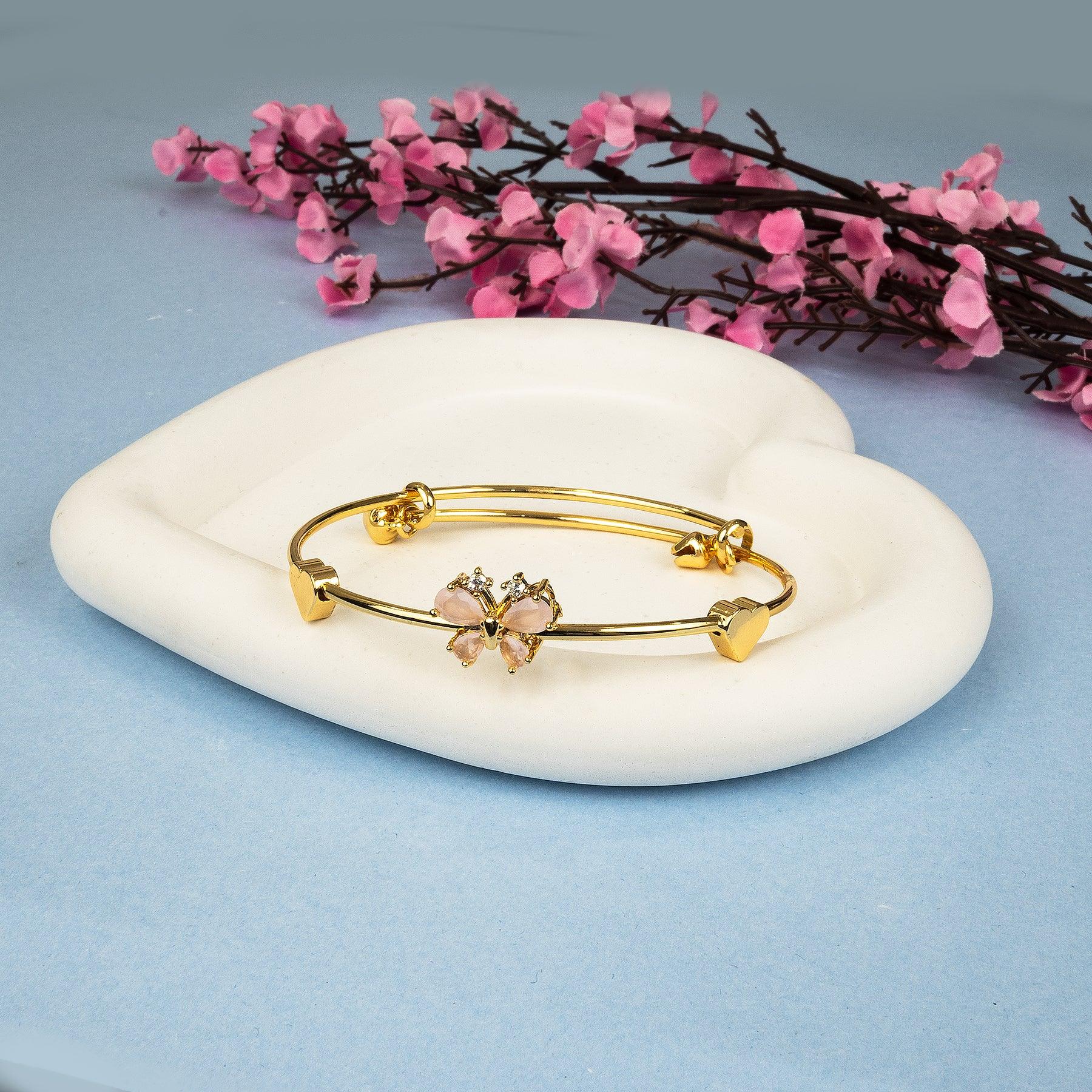 Gold bracelet with pink stones on a white dish with pink flowers in the background