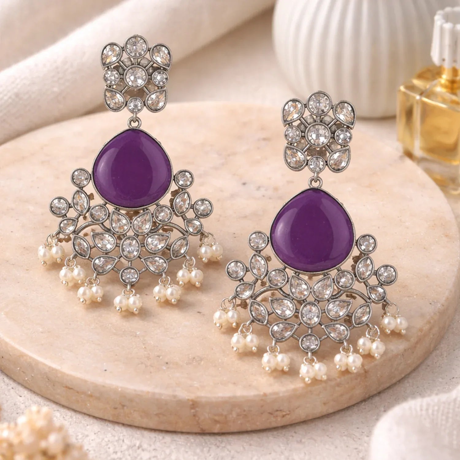 Purple earrings with silver and pearl details on a wooden surface.