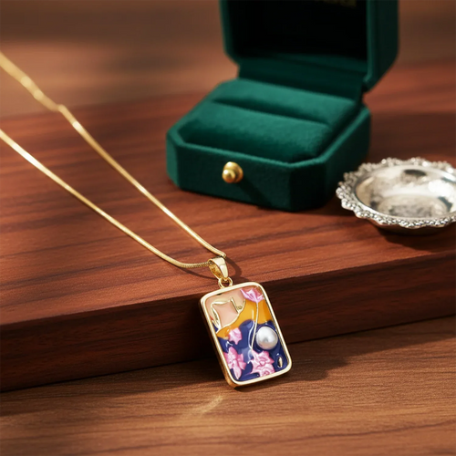Gold necklace with a decorative pendant on a wooden surface with a green jewelry box in the background.