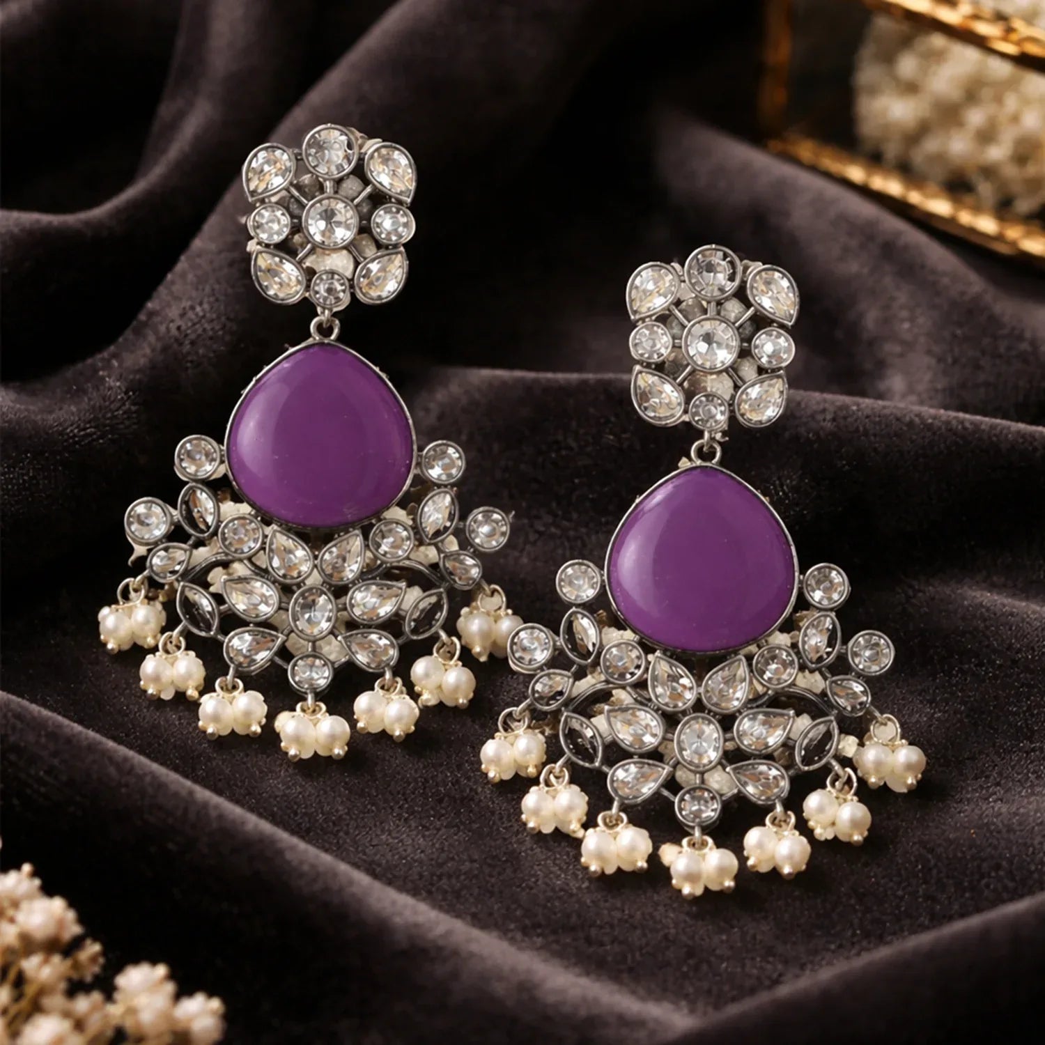 Purple gemstone earrings with silver and pearl details on a dark fabric background
