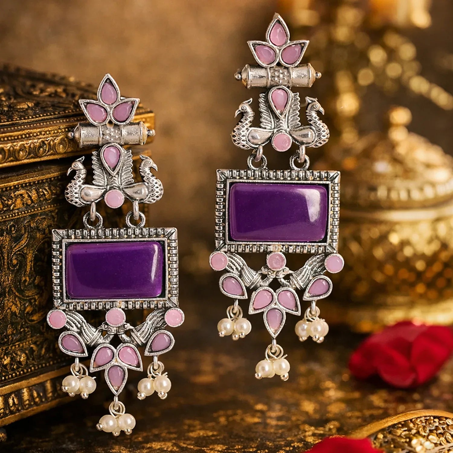 Ornate earrings with purple stones and pink accents on a decorative background