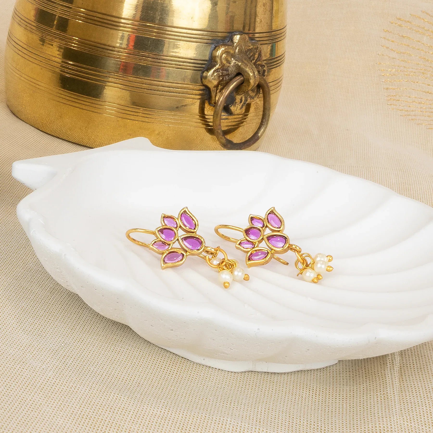 Gold and purple earrings on a white dish with a gold container in the background.