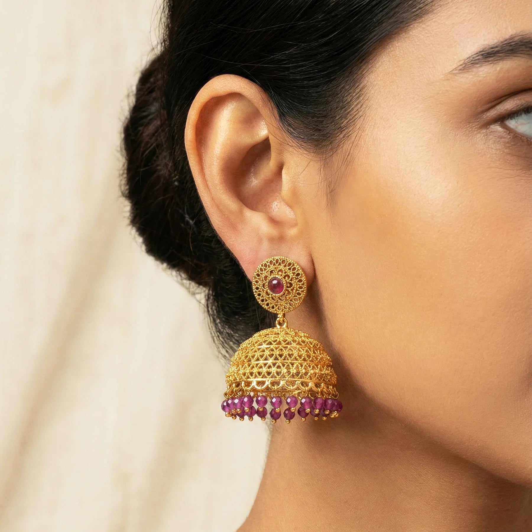 Gold and purple earrings worn by a person with a neutral background