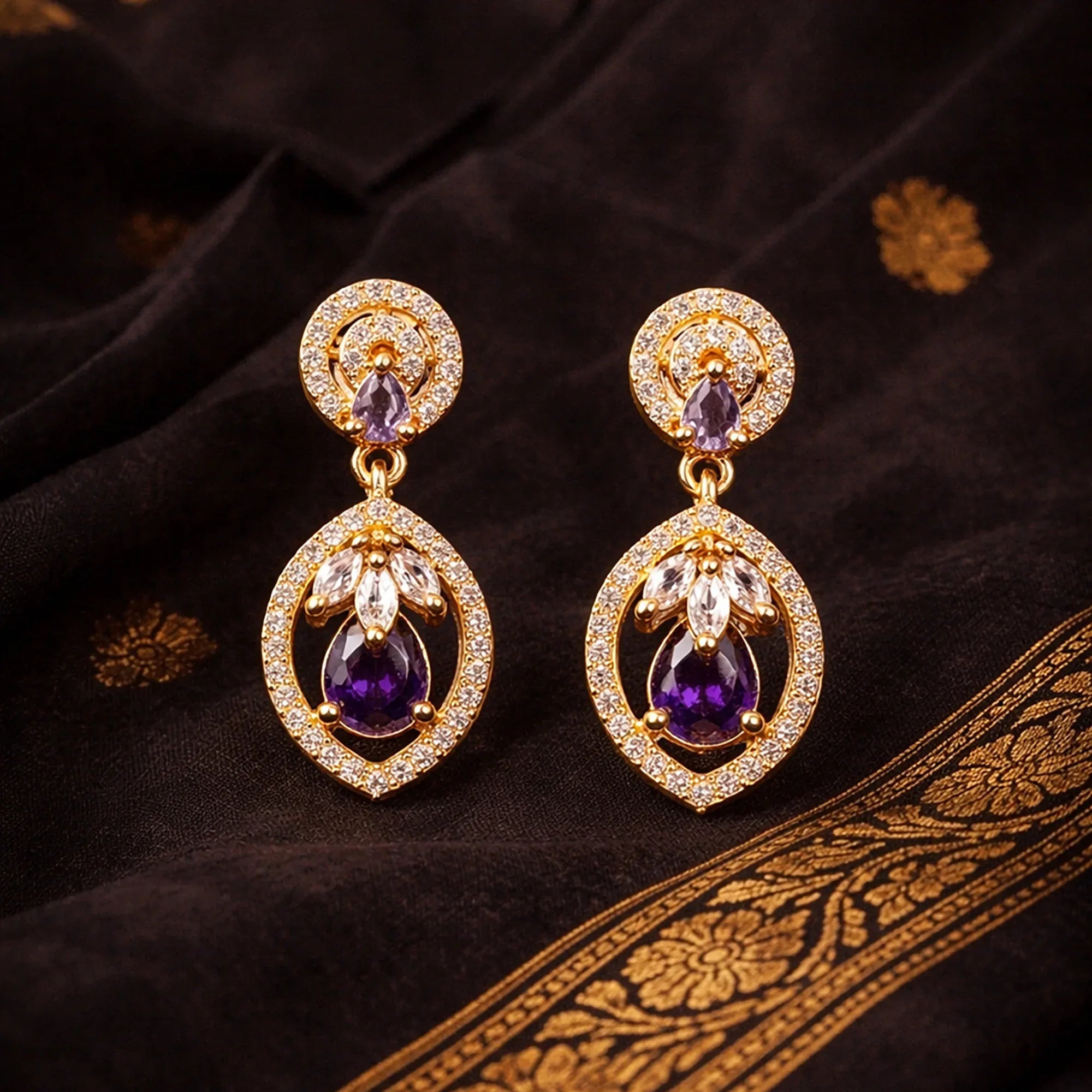 Pair of gold earrings with purple gemstones on a dark fabric background