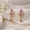 Gold earrings with purple gemstones on a beige fabric background