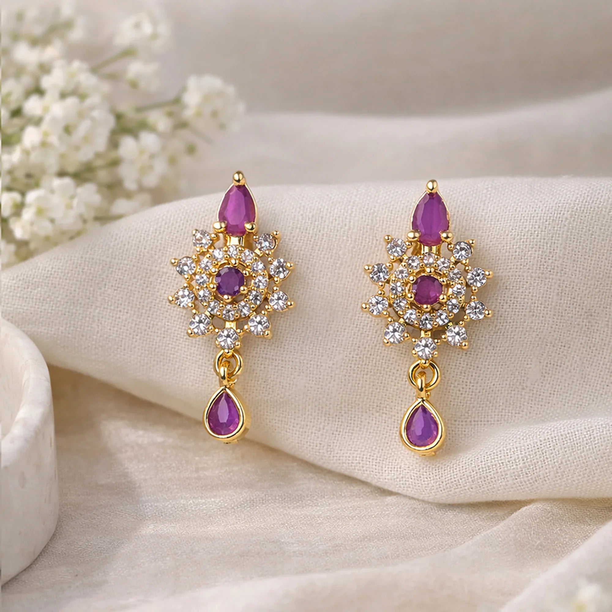 Gold earrings with purple gemstones on a beige fabric background