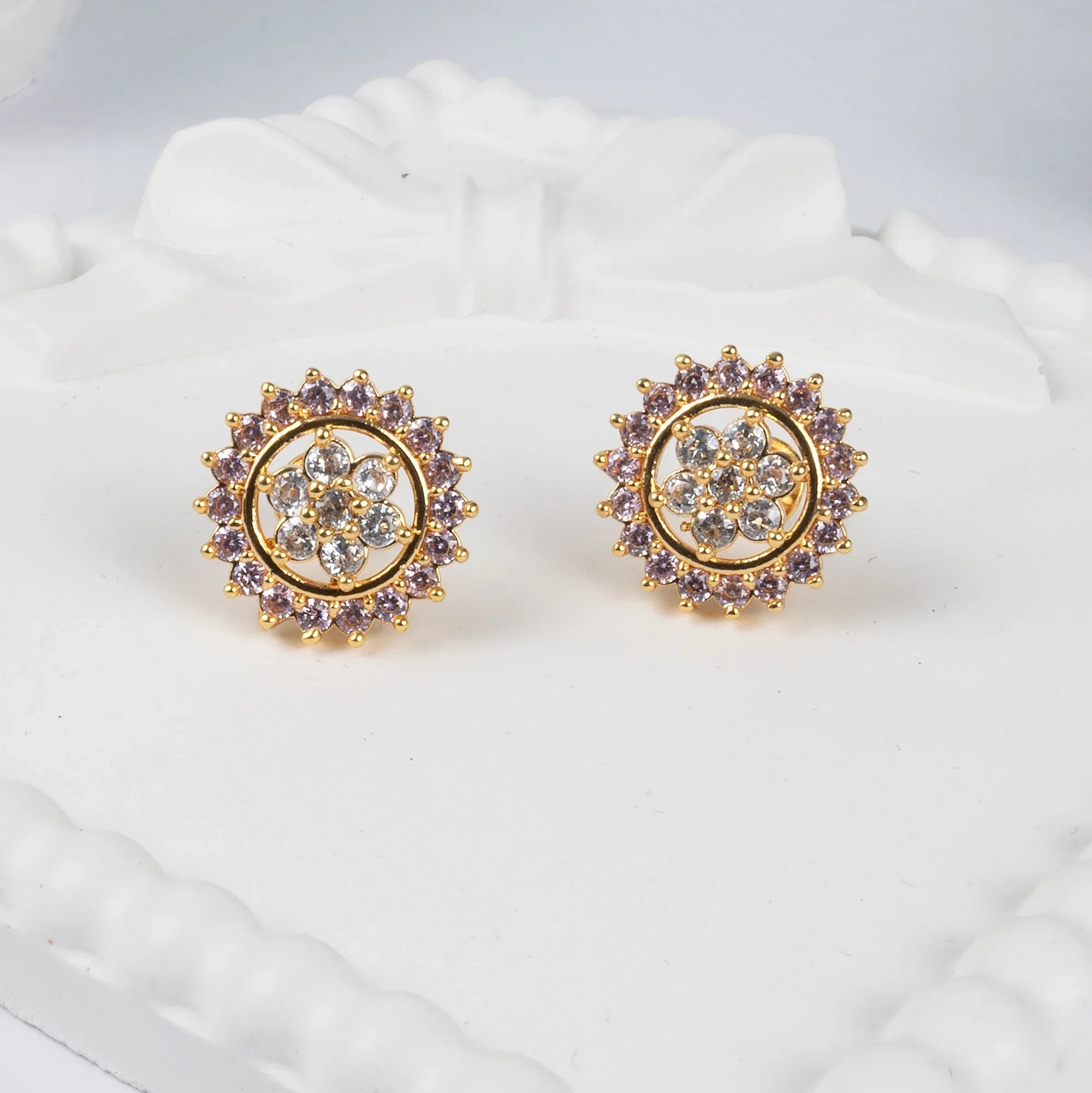 Gold earrings with purple and clear gemstones on a white cushion