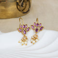Gold earrings with purple gemstones and pearl drops on a white surface.