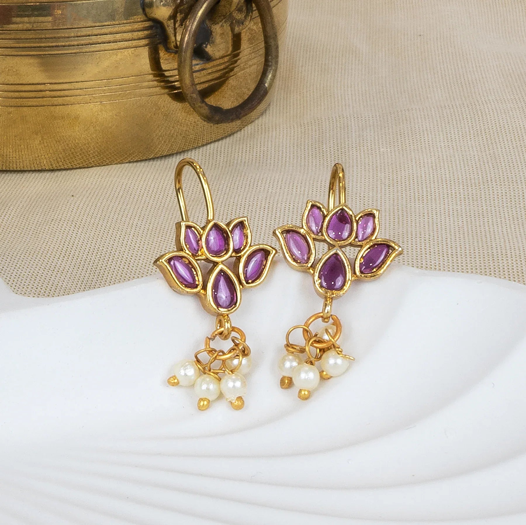 Gold earrings with purple gemstones and pearl drops on a white surface.