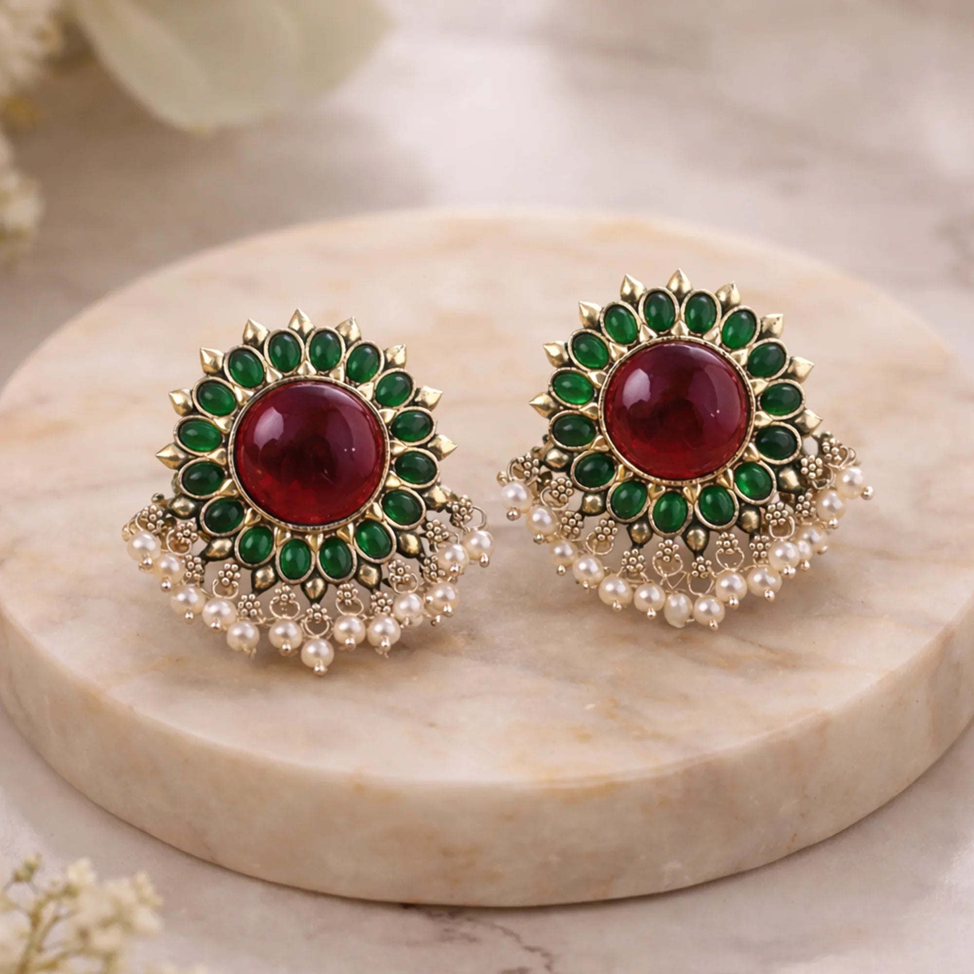 Pair of ornate earrings with red and green stones on a marble surface