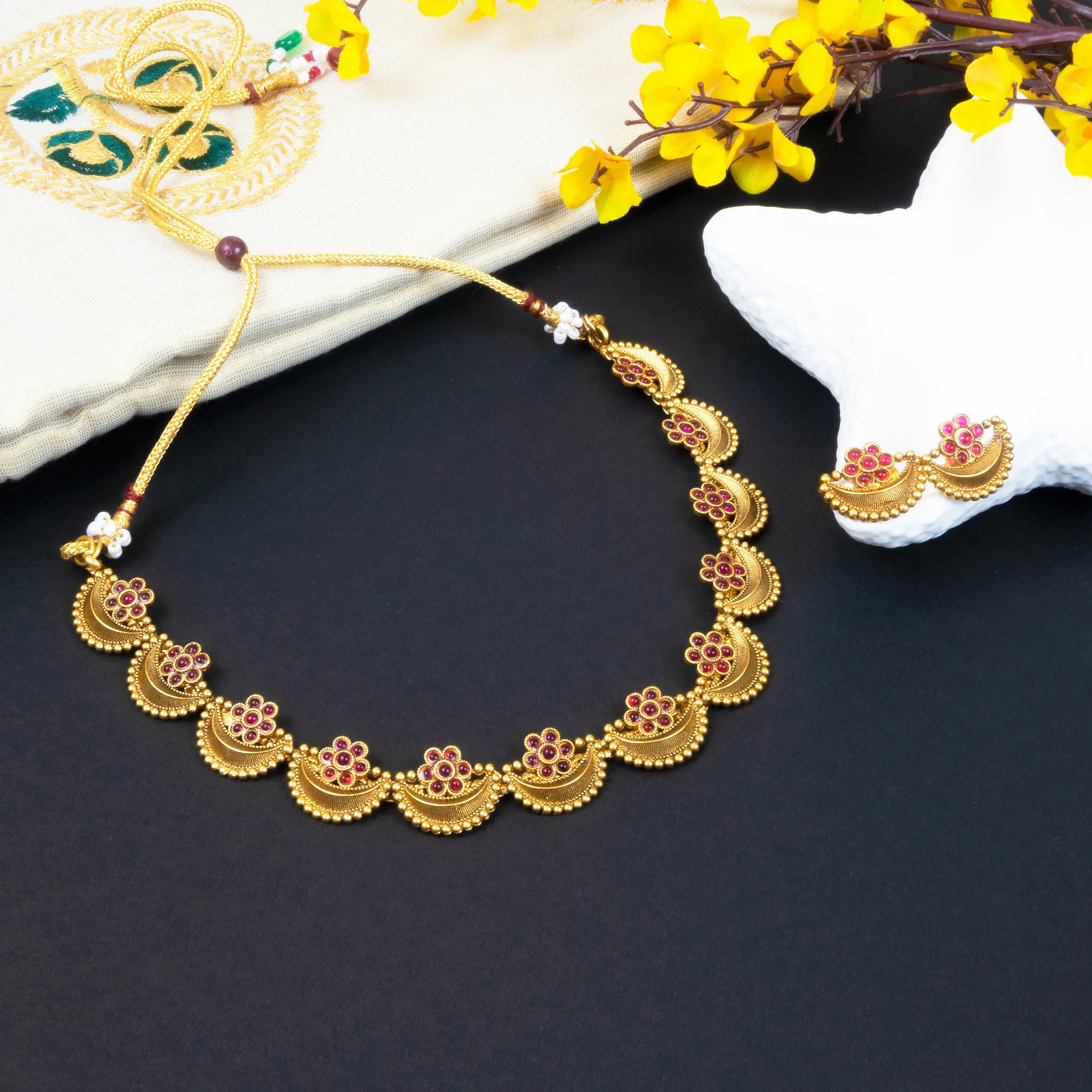 Gold necklace with floral designs on a dark surface with yellow flowers in the background