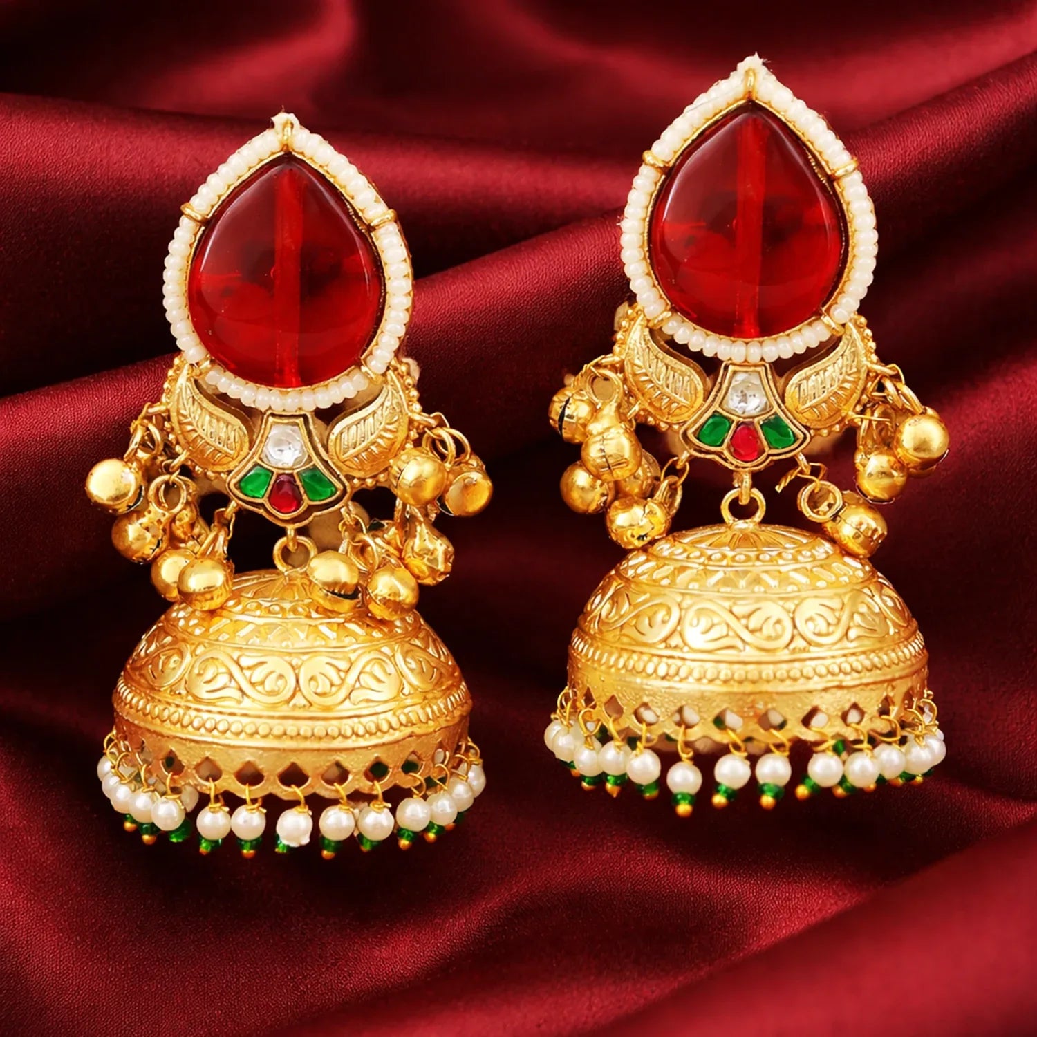 Ornate gold earrings with red gemstones on a red fabric background