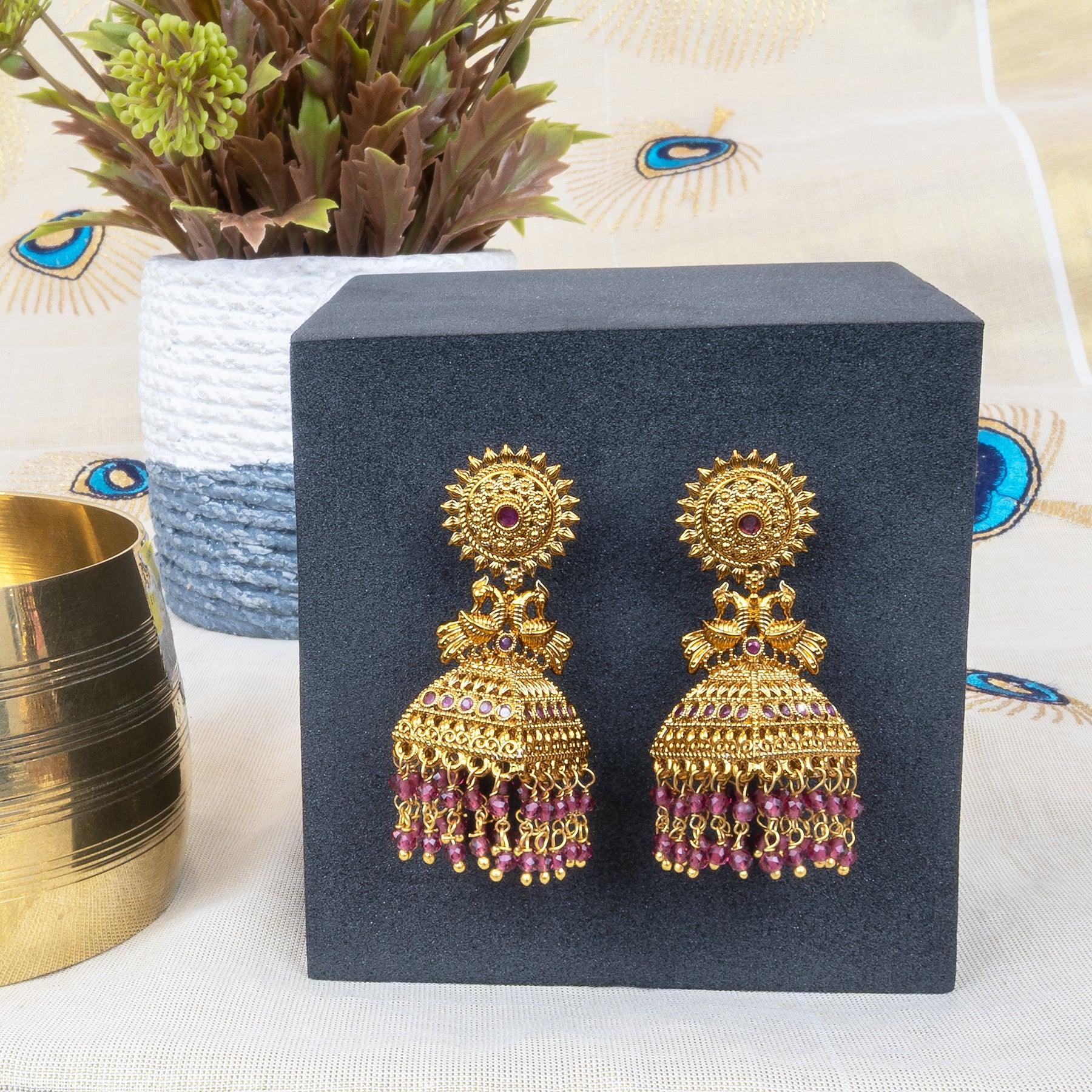 Gold and pink earrings on a black stand with a decorative background