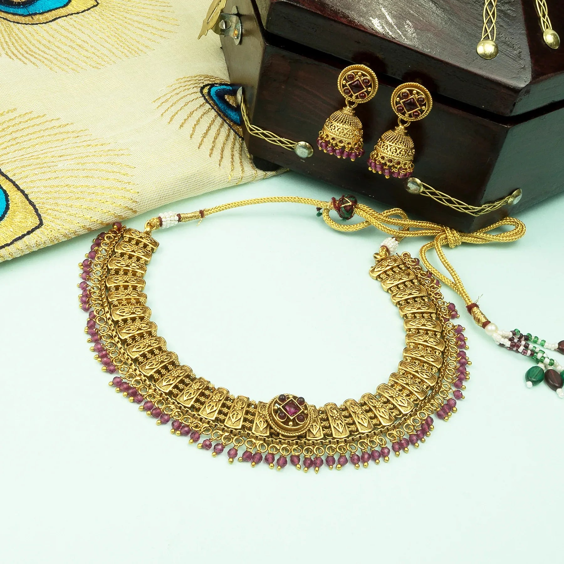 Gold necklace with pink stones and matching earrings on a light green surface.