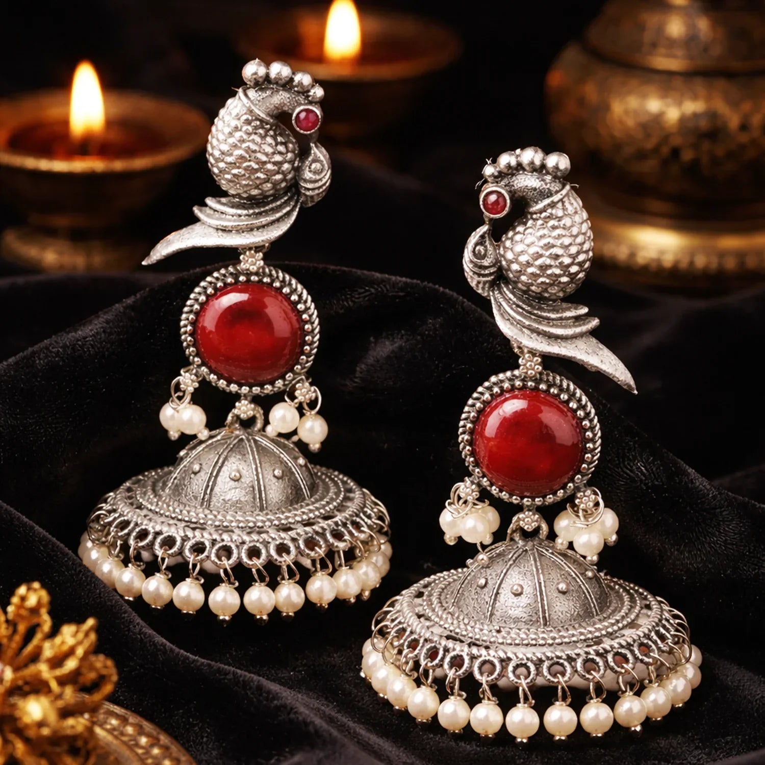 Ornate silver and red earrings with pearl accents on a dark fabric background.