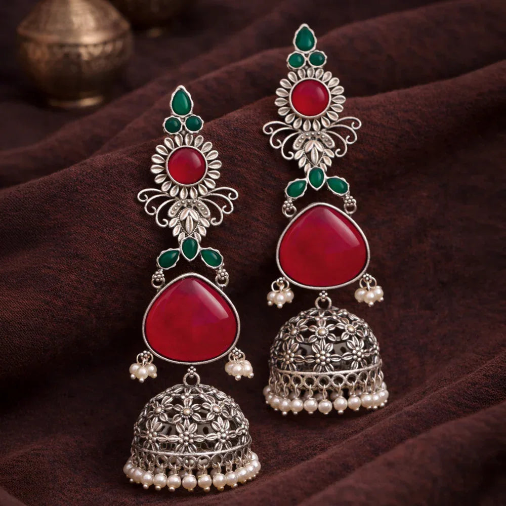 Ornate earrings with red stones and silver detailing on a dark fabric background