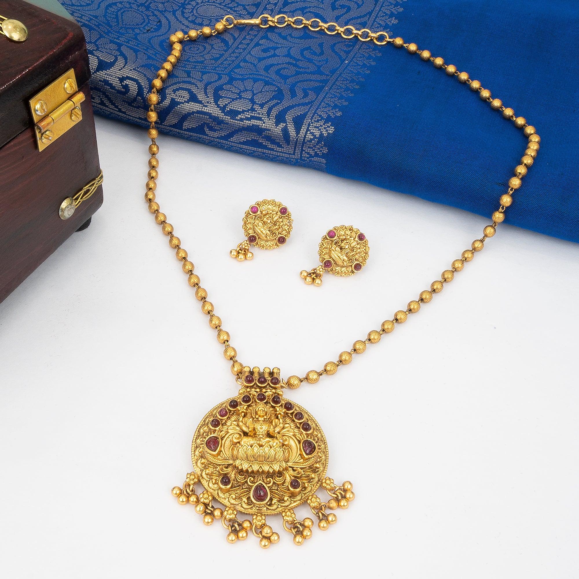 Gold necklace with pendant and matching earrings on a white surface with a blue fabric background