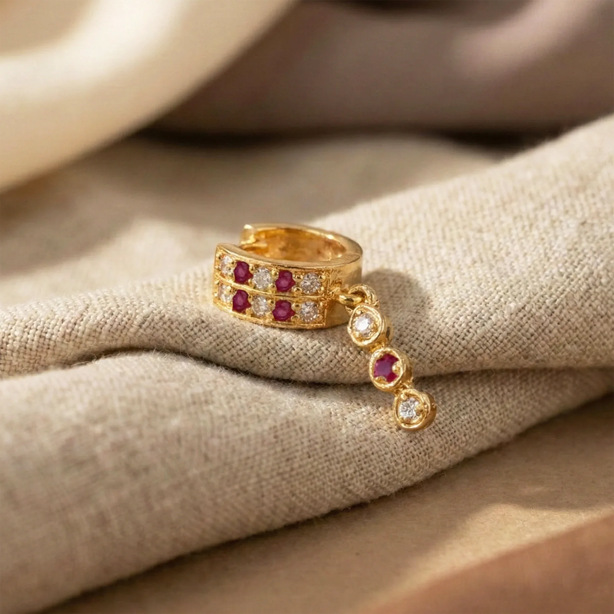 Gold ring with red gemstones and small diamonds on a beige fabric background