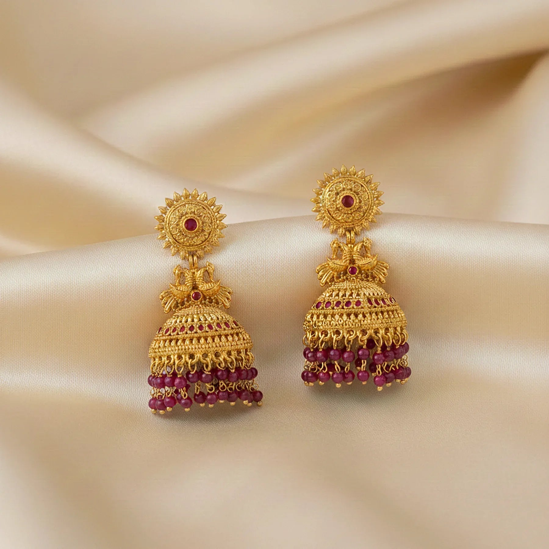 Gold earrings with red gemstones on a beige fabric background