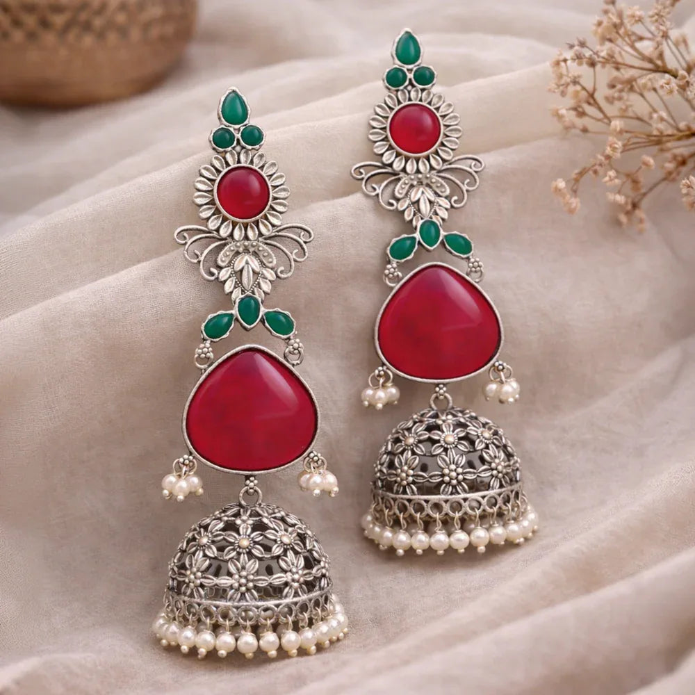 Ornate earrings with red stones and silver detailing on a soft fabric background