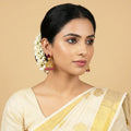 Woman wearing a cream saree with gold border and floral hair accessory on beige background