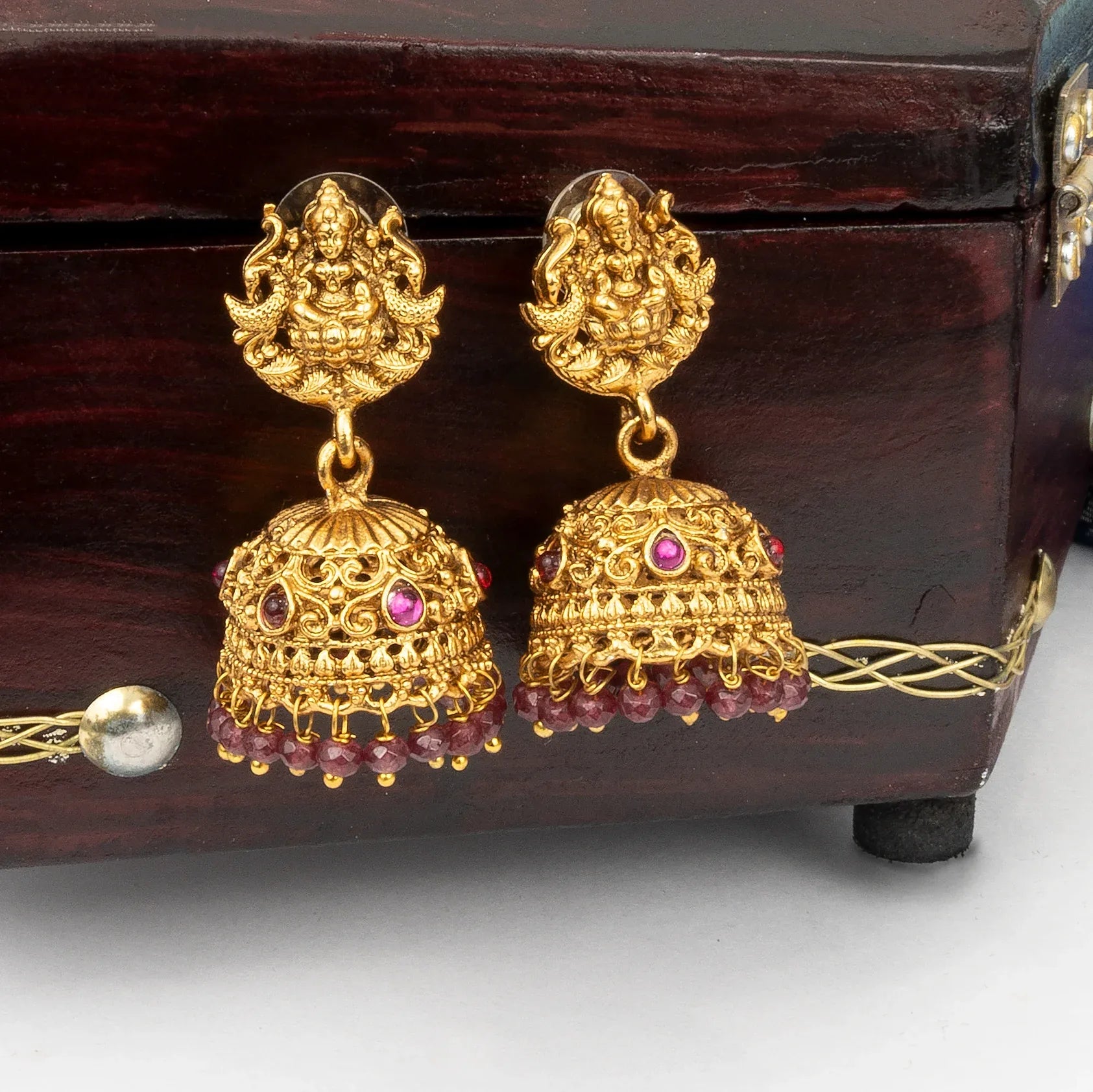Gold earrings with intricate designs and red stones on a wooden box.
