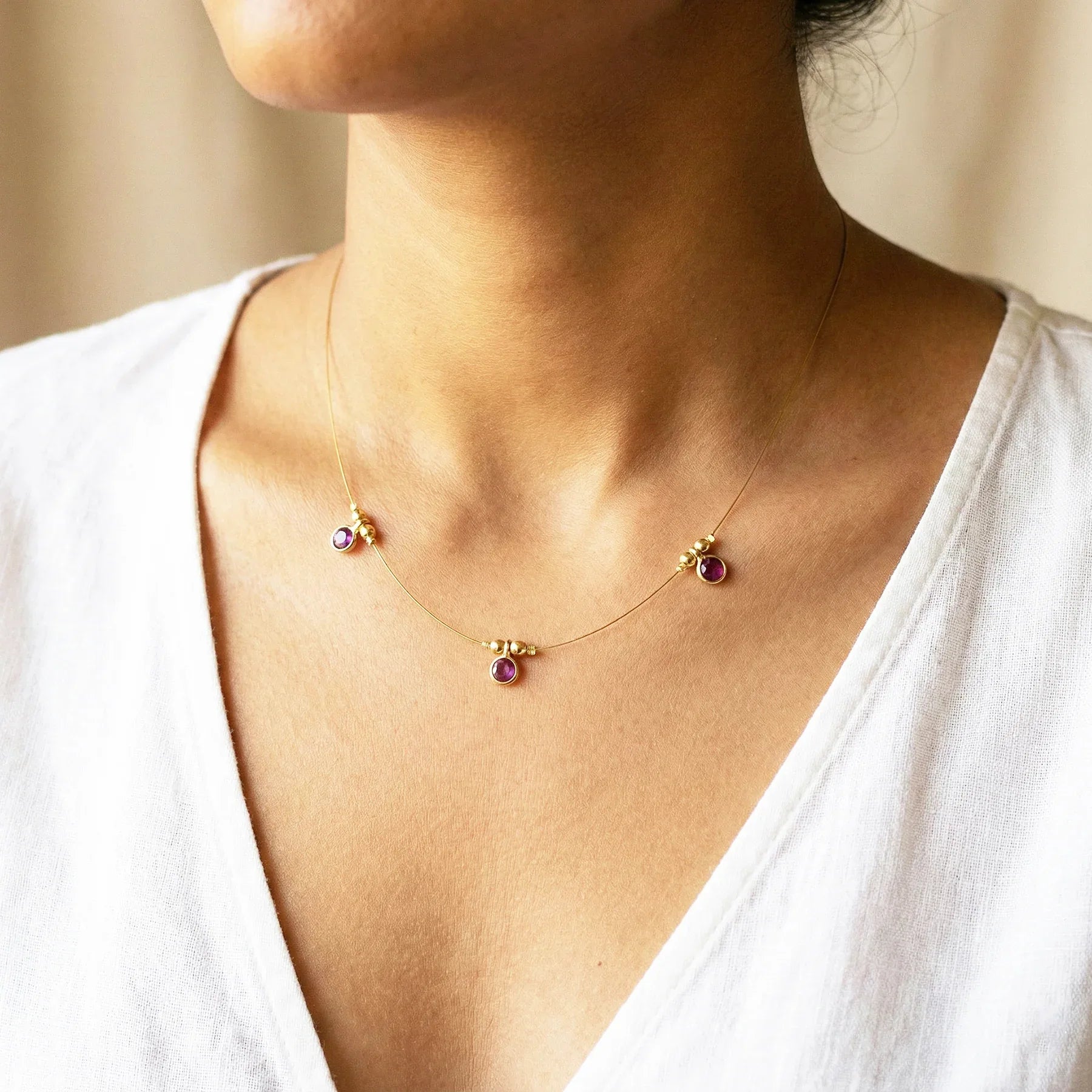 Necklace with small round pendants on a person wearing a white top.