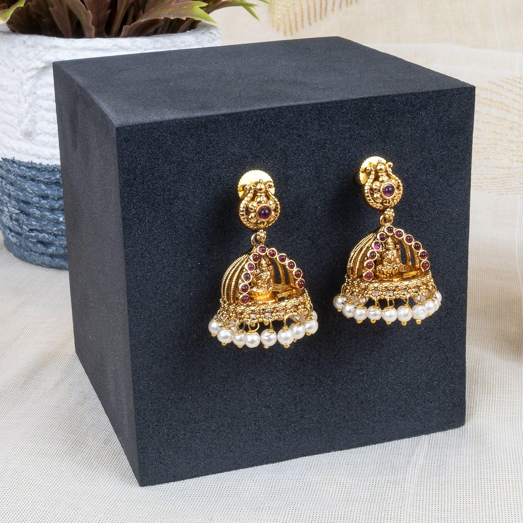Gold and pearl earrings on a black stand with a blurred background