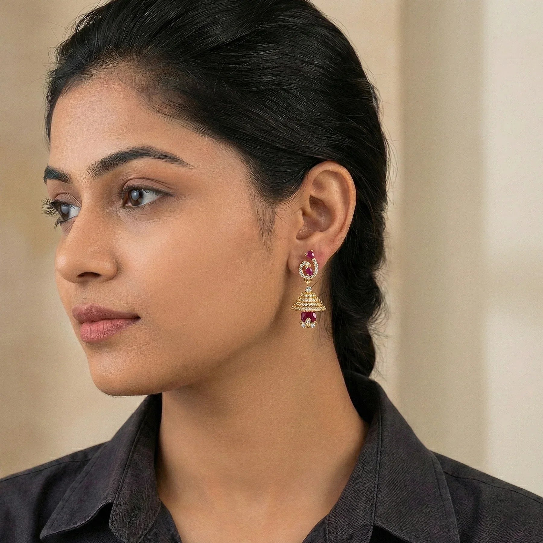Woman wearing gold earrings with red stones against a neutral background