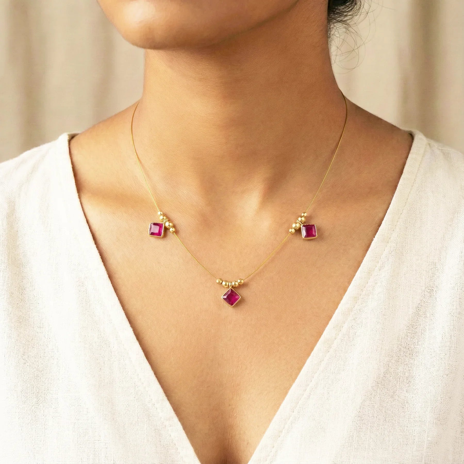 Necklace with pink gemstones worn by a person in a white top.
