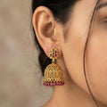 Gold earrings with red gemstones worn by a person against a neutral background