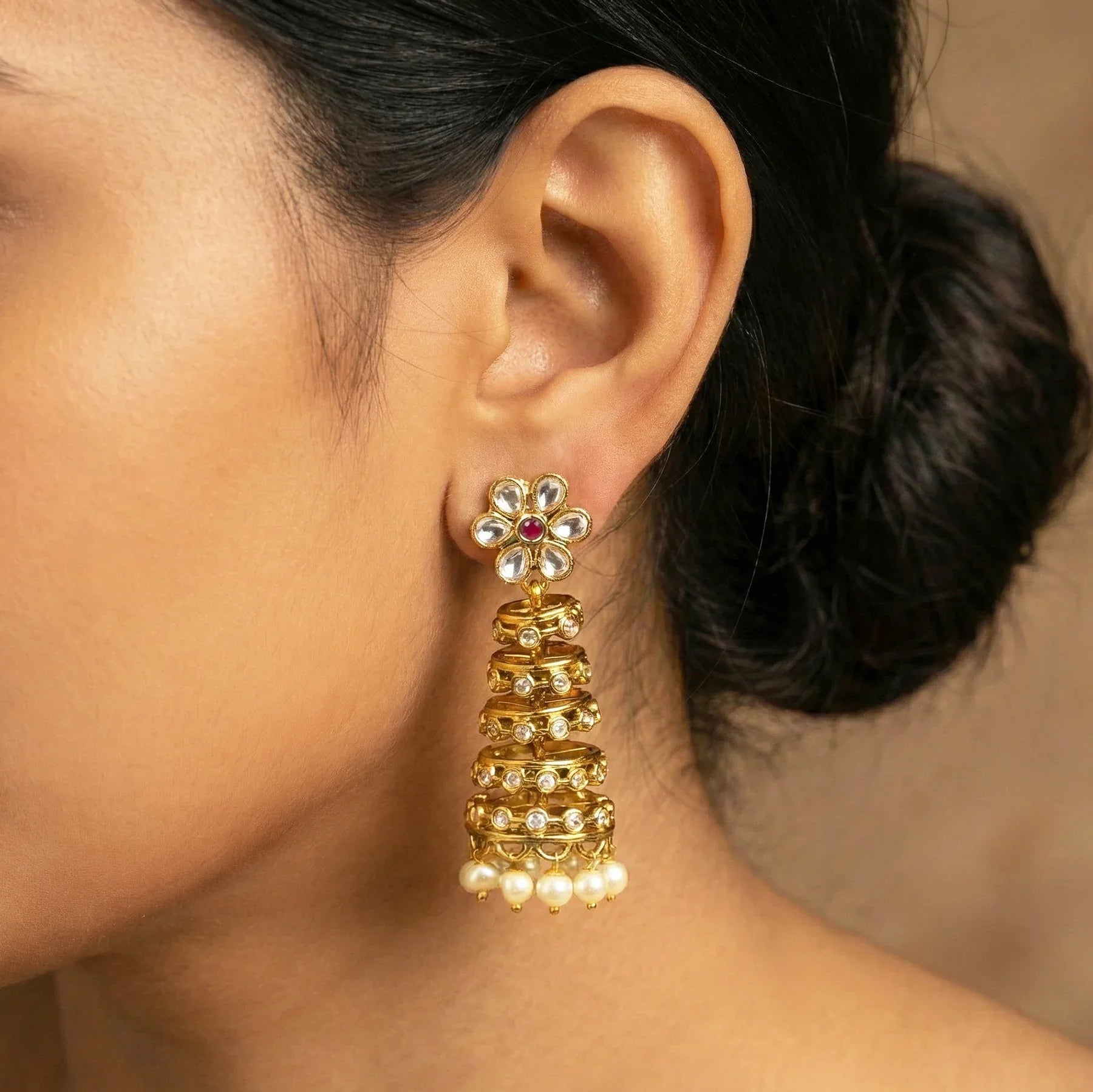 Close-up of a person wearing a gold earring with floral design and pearl details.