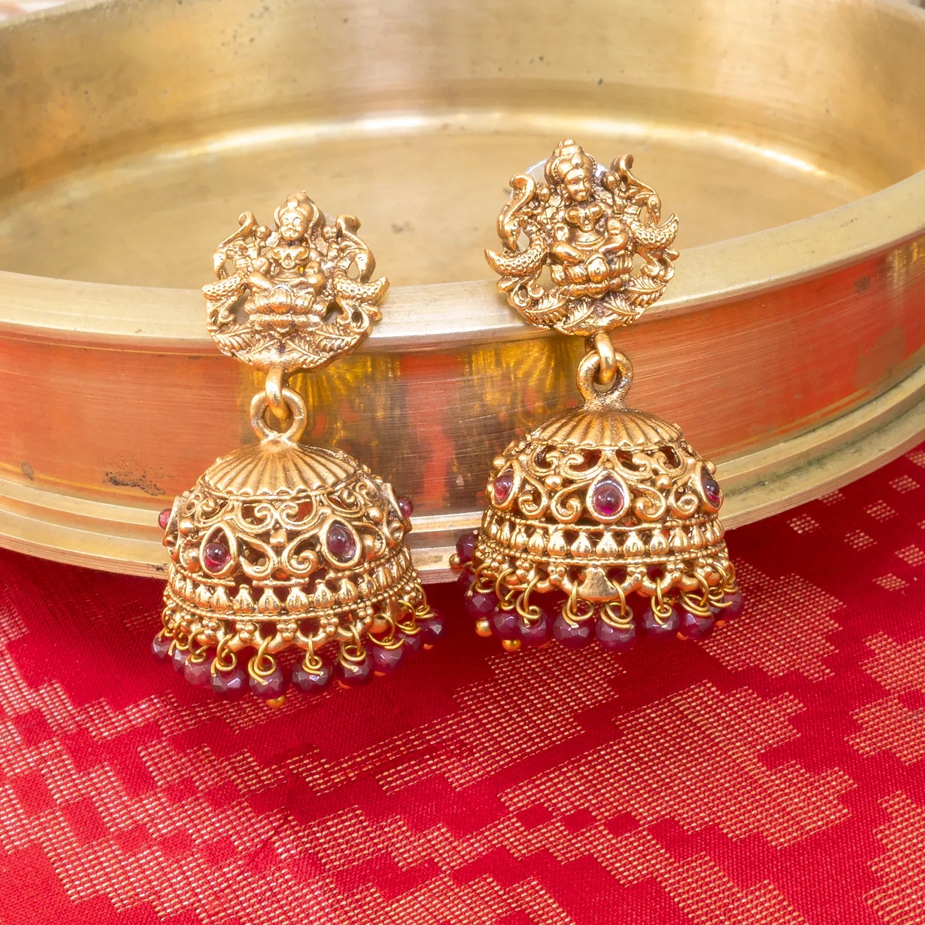 Gold earrings with red stones on a red fabric background
