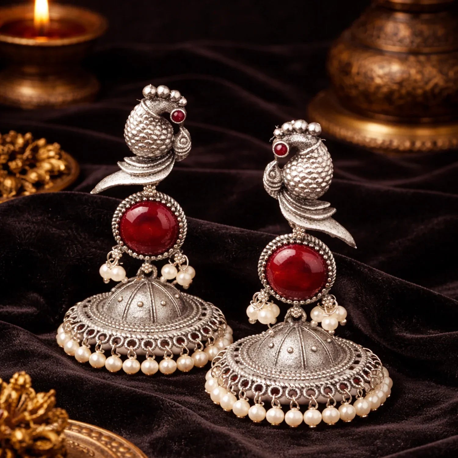 Pair of silver and red earrings with pearl accents on a dark fabric background