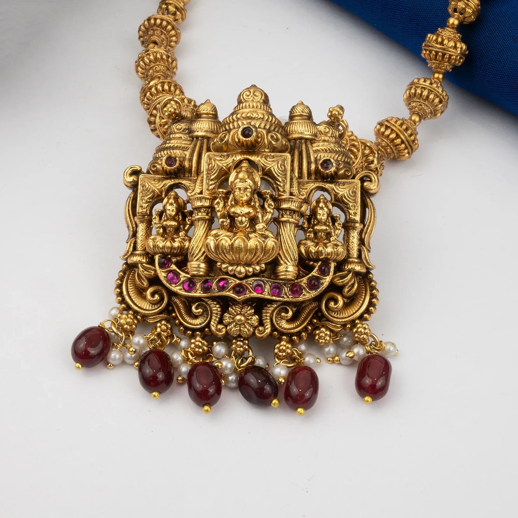 Gold necklace with intricate design and red stones on a white background