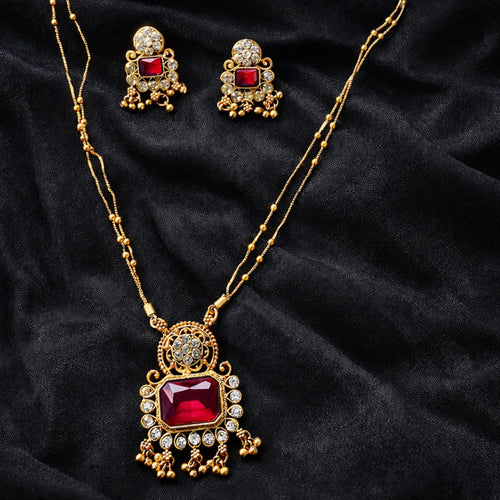 Gold necklace with red gemstone and matching earrings on a black fabric background