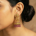 Close-up of a person wearing a gold and purple earring with a blurred background