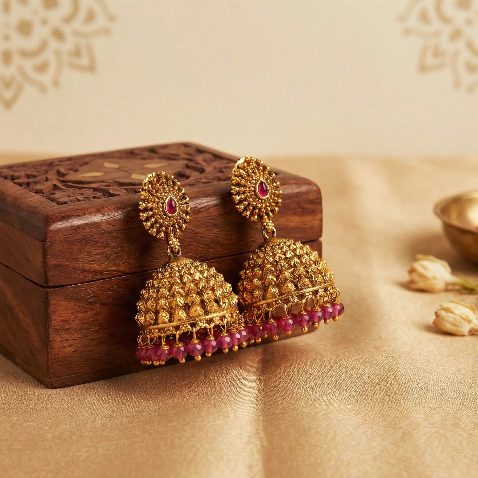 Gold earrings with red gemstones on a wooden box