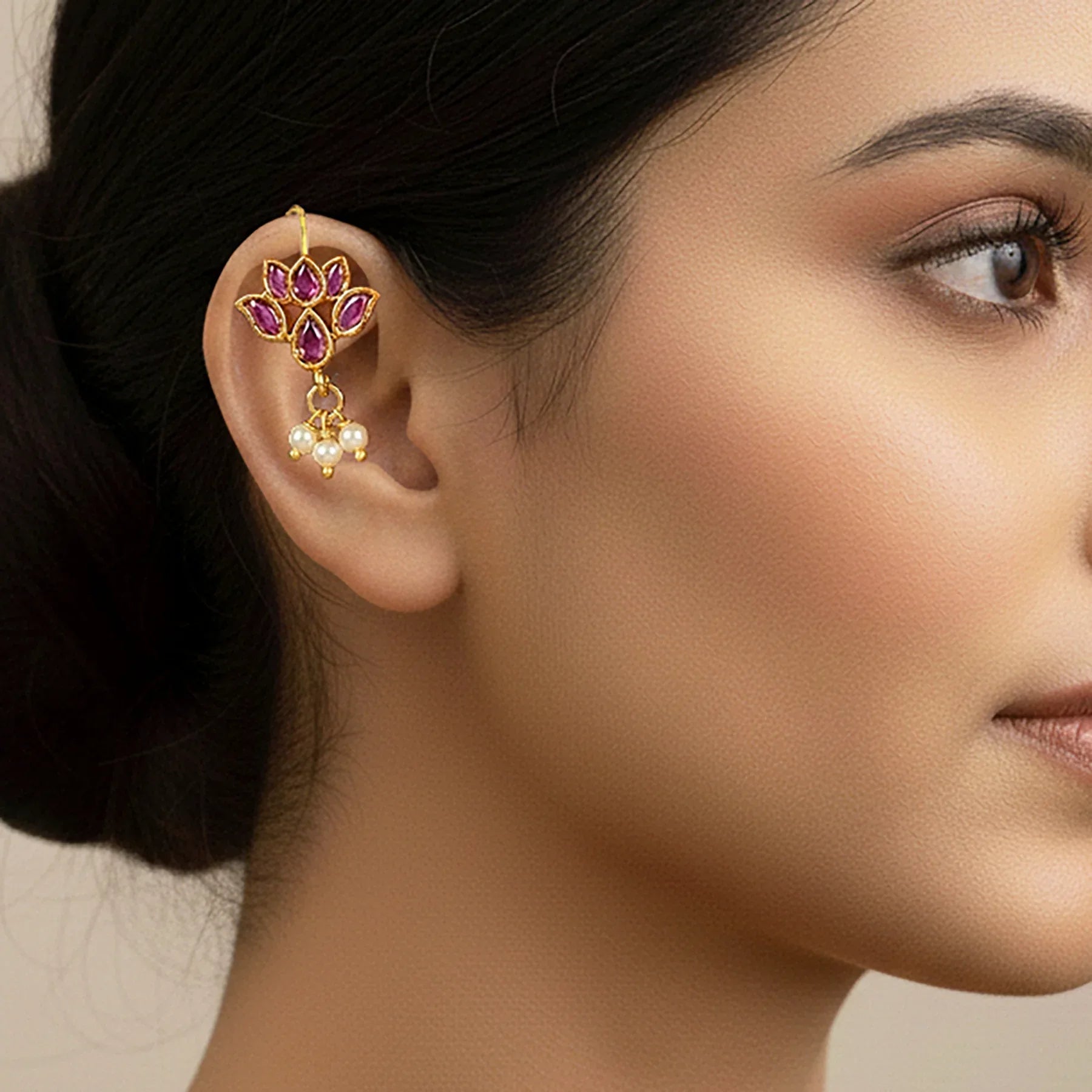 Close-up of a woman wearing a gold and purple floral earring with pearl drops.