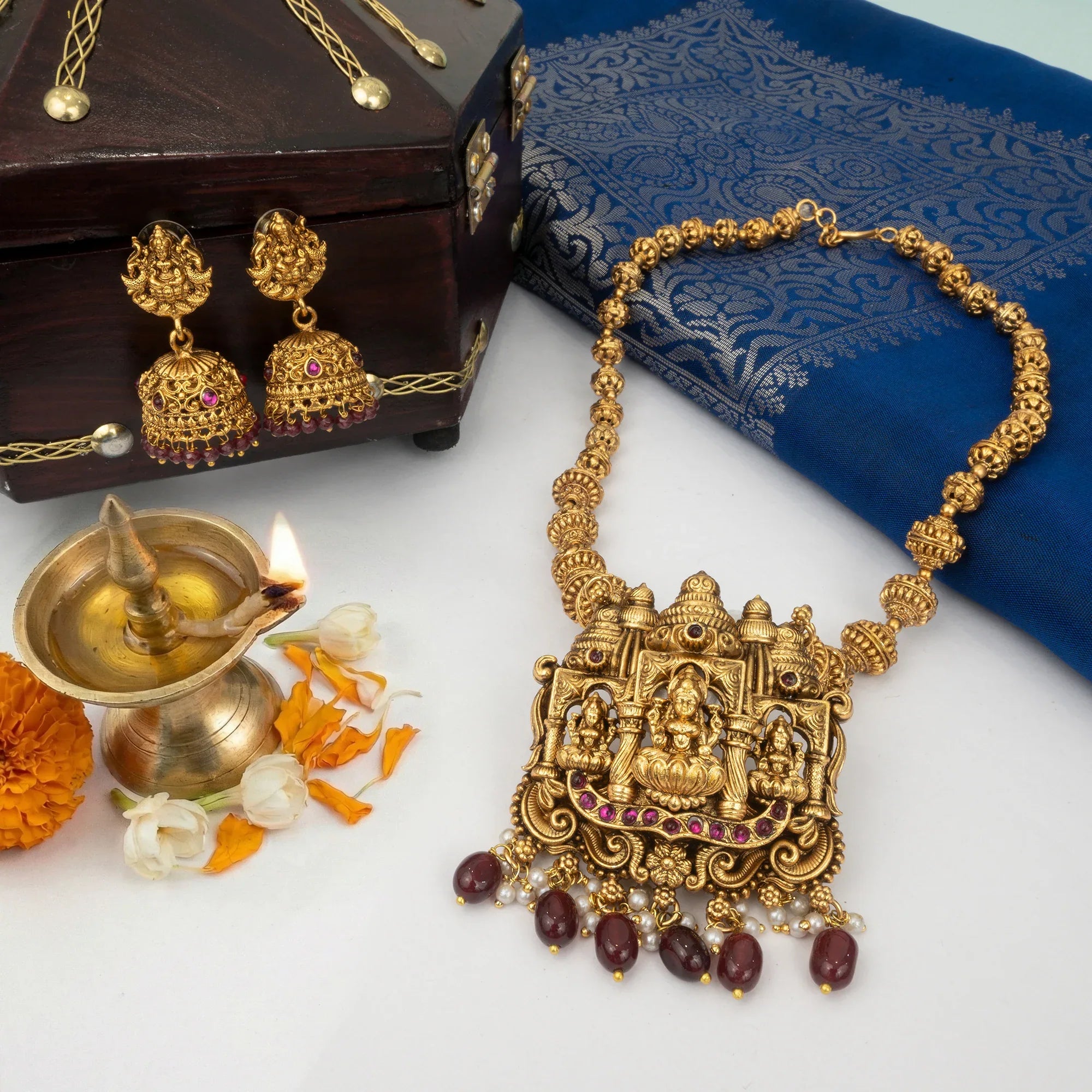 Gold necklace with intricate design on a white surface with a blue fabric and lit lamp in the background.