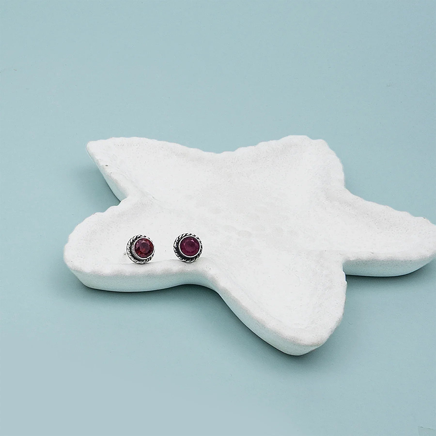 Pair of star-shaped earrings on a white star-shaped stand against a light blue background