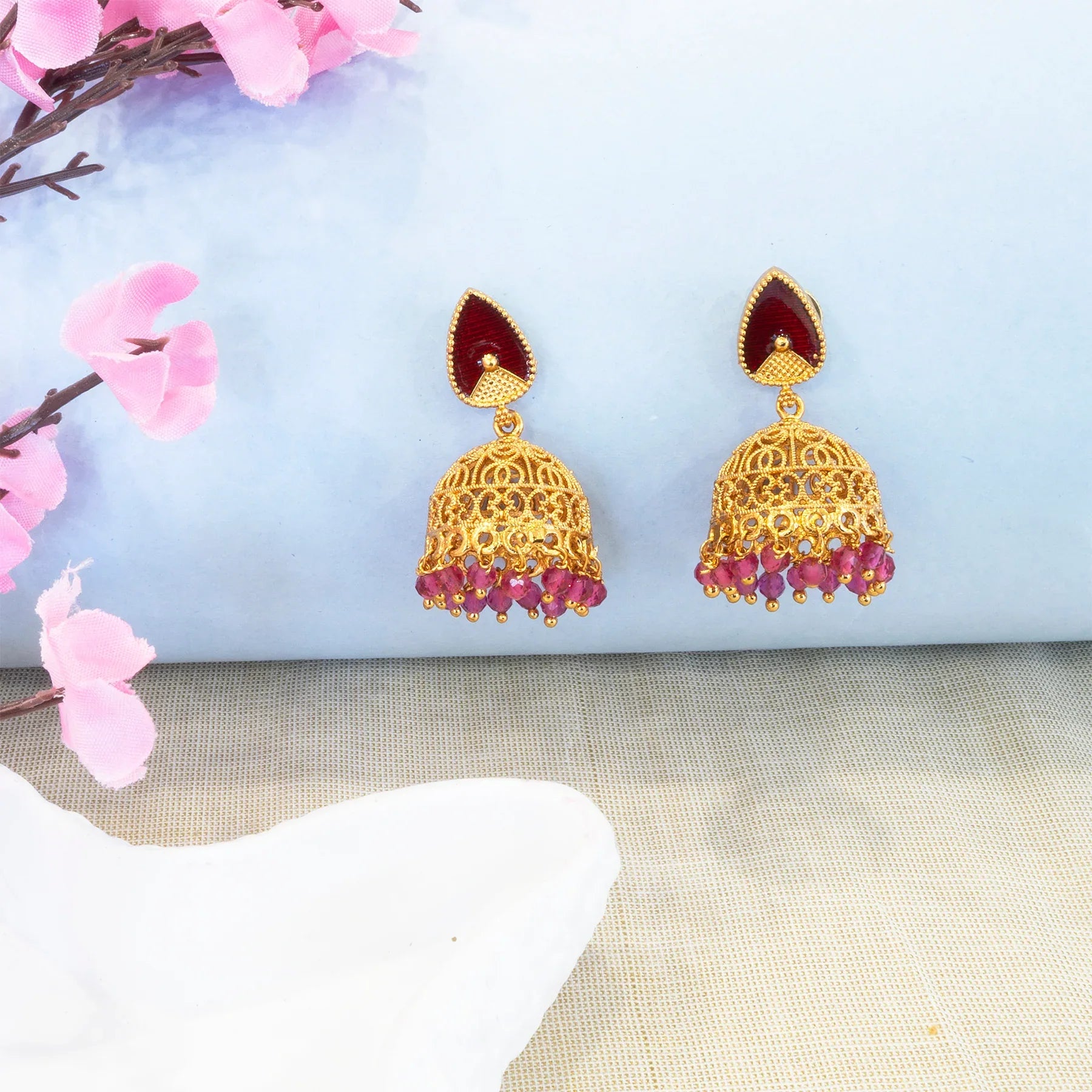 Gold earrings with red stones on a light blue fabric background with pink flowers.