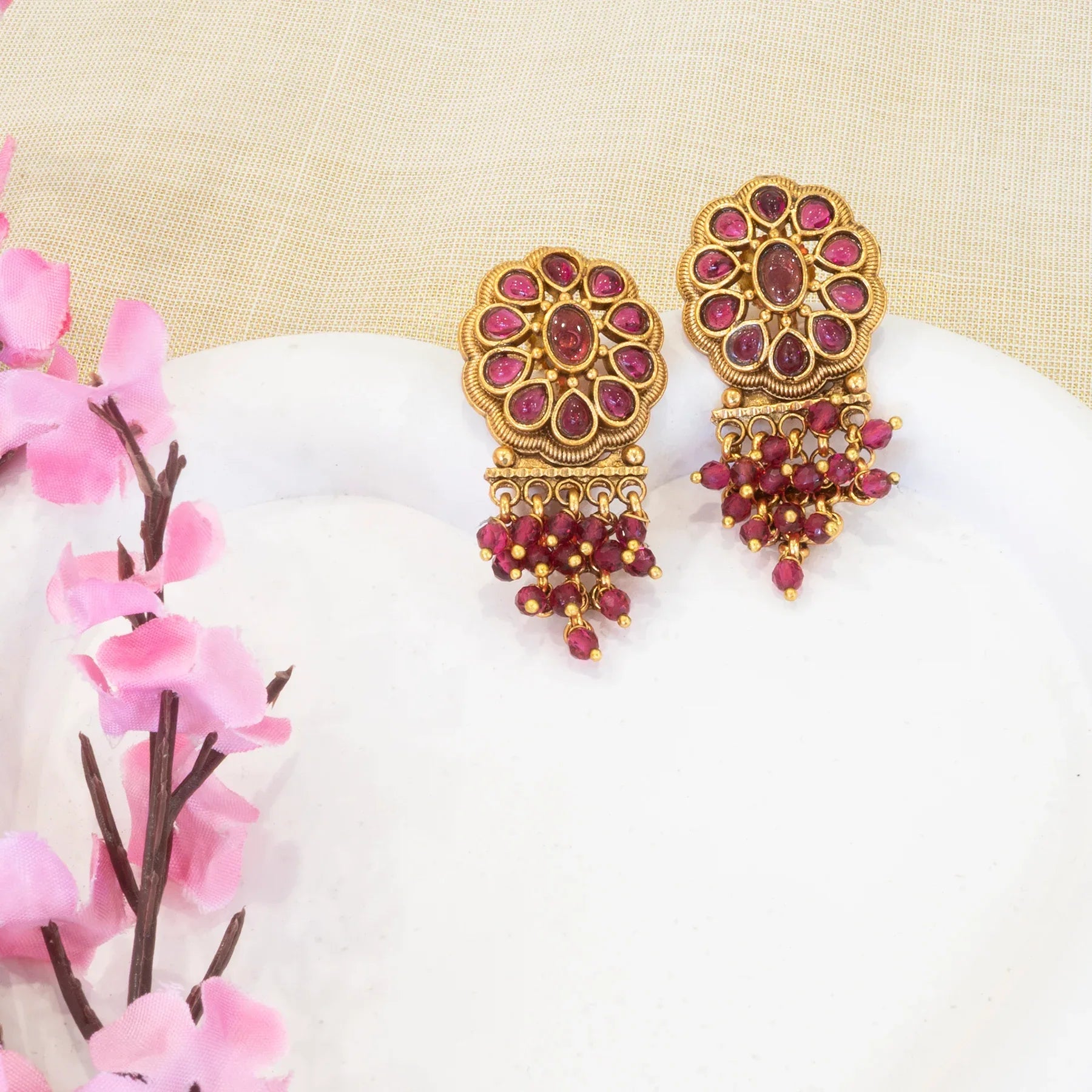 Gold and red earrings on a white surface with pink flowers in the background