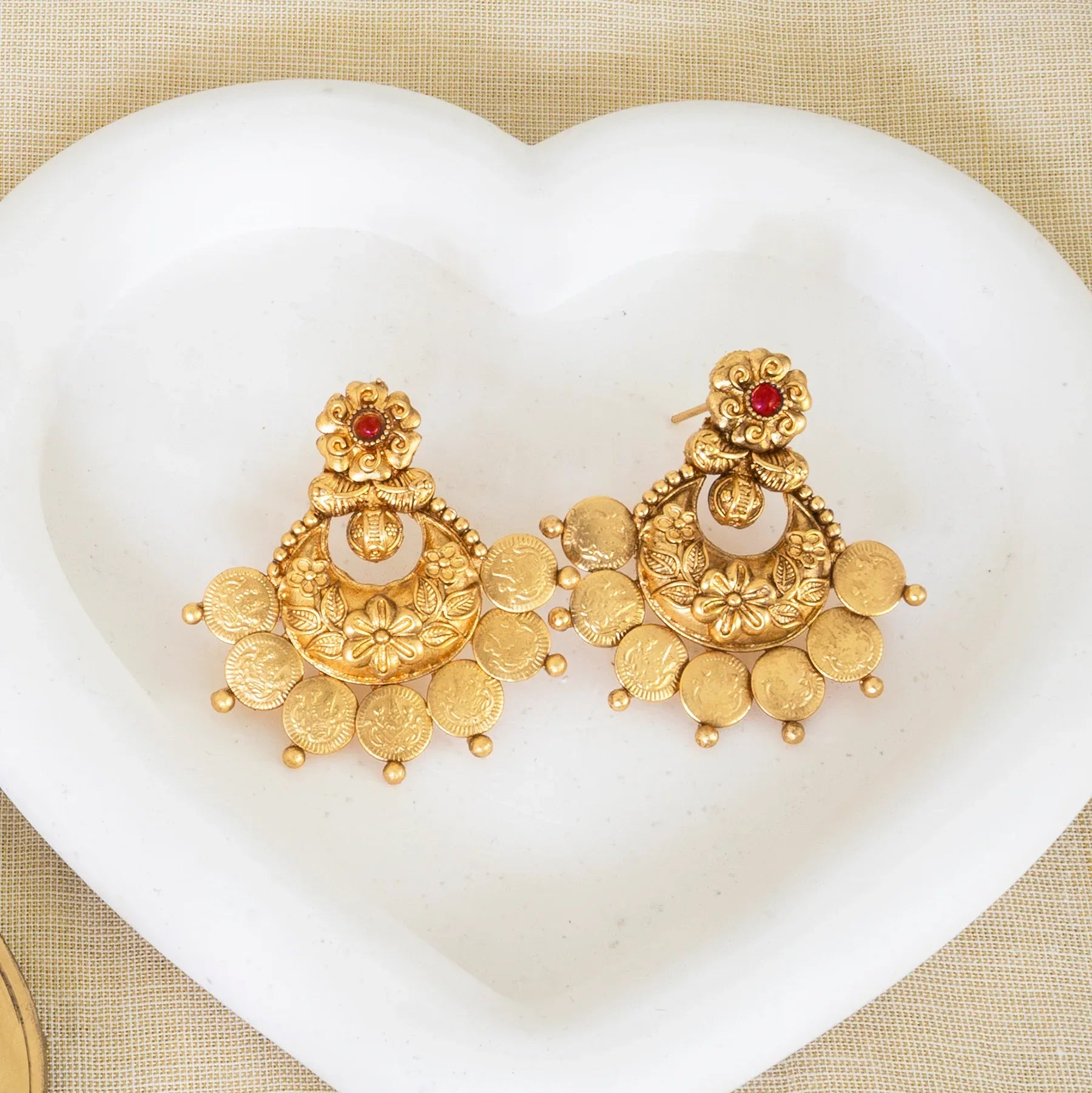 Gold earrings with red stones on a white heart-shaped pillow