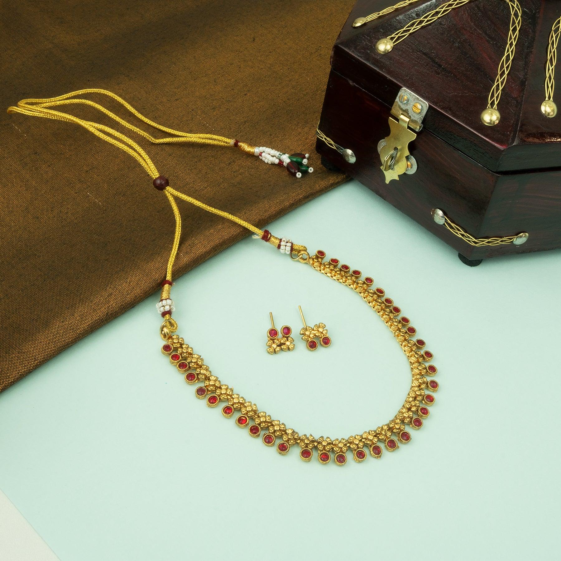 Gold necklace with red stones and matching earrings on a green surface with a wooden box.