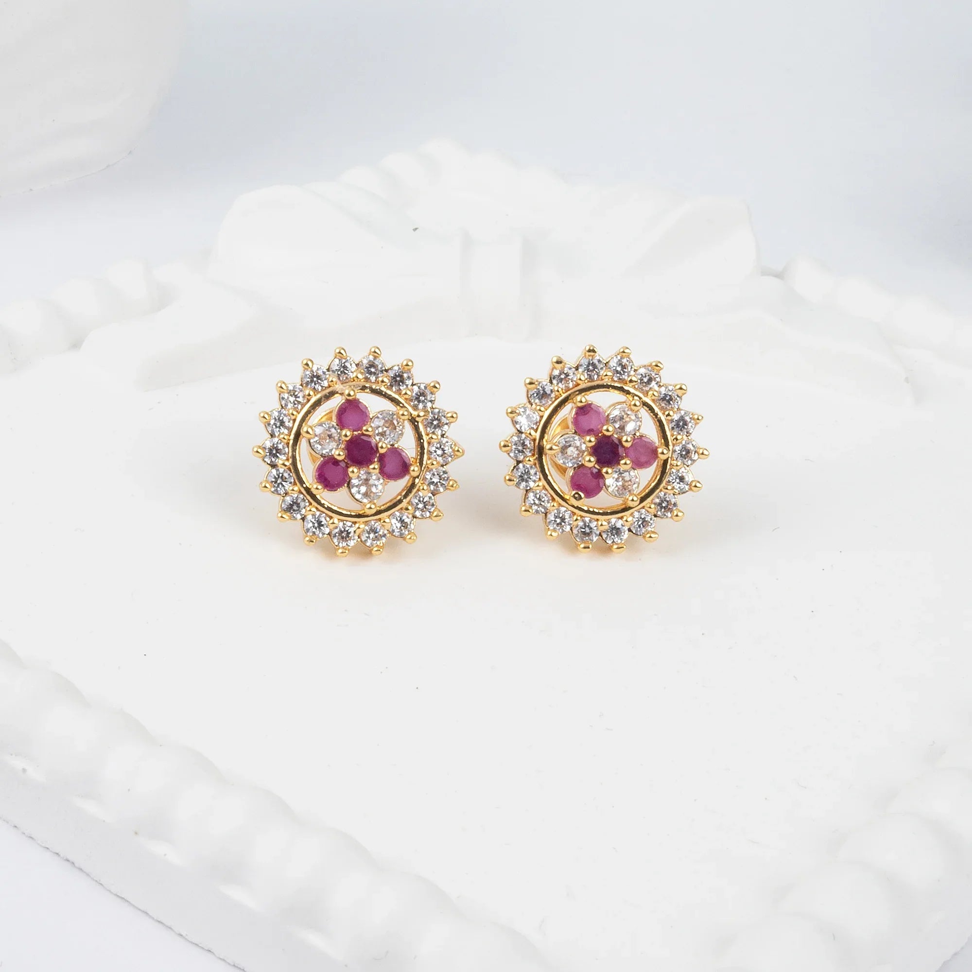 Gold earrings with red gemstones and clear stones on a white surface