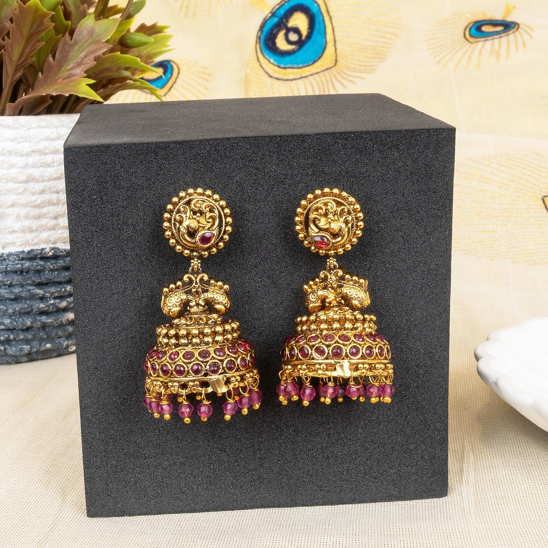 Gold and red earrings on a black display box with peacock feather decorations.