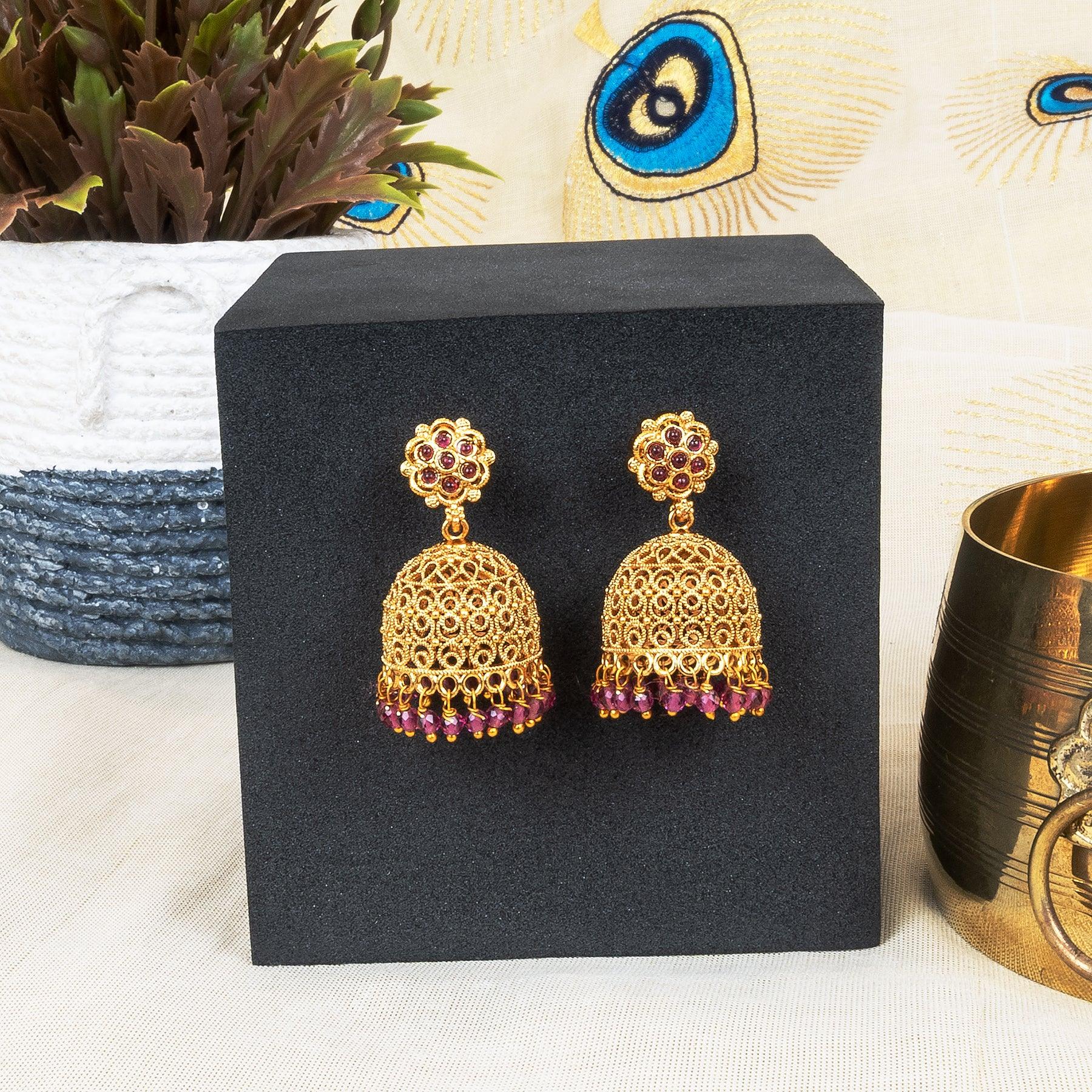 Gold earrings with red stones on a black stand, with decorative items in the background.